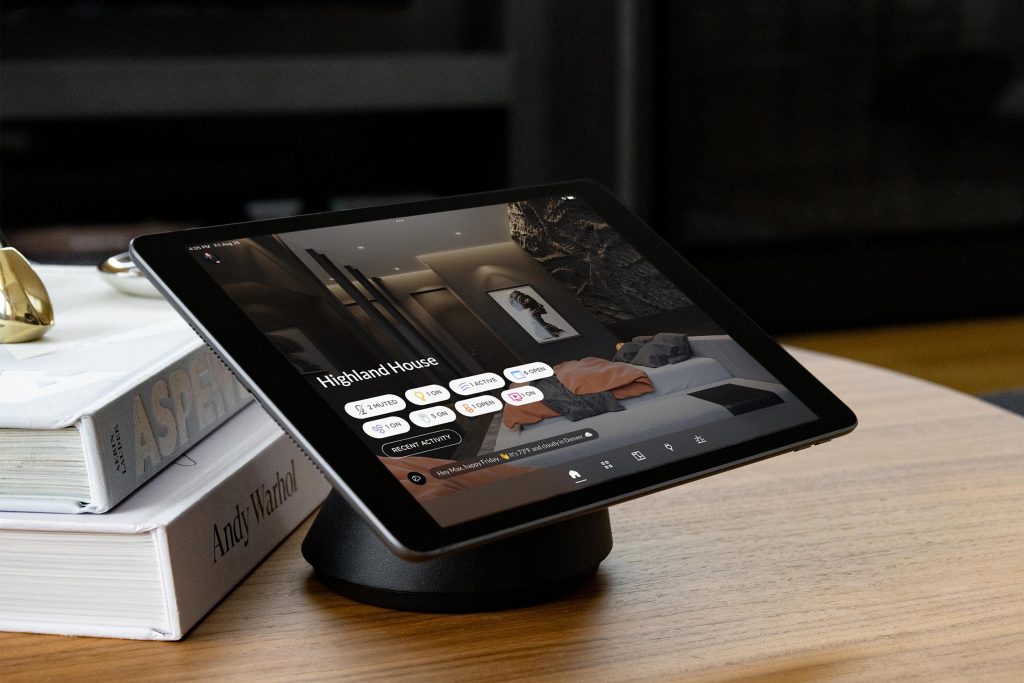 Tablet displaying the Josh.ai smart home app interface with circular voice command icons and control options for lighting, music, and scenes on a sleek, dark-themed dashboard.
